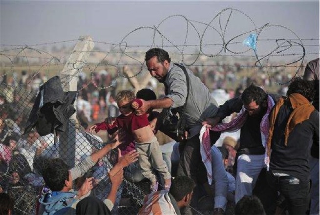 In this Sunday, June 14, 2015 file photo, a Syrian refugee carries a baby over the broken border fence into Turkey after breaking the border fence and crossing from Syria in Akcakale, Sanliurfa province, southeastern Turkey. A Kurdish official says a new administration has been formed for a majority Sunni-Arab town controlled by Syrian Kurds, expanding the ethnic group’s semi-autonomous administration in northern Syria. (AP Photo/Lefteris Pitarakis, File)