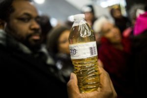 Pastor David Bullock holds up a bottle of Flint water as Michigan State Police hold a barrier to keep protestors out of the Romney Building, where Gov. Rick Snyder's office resides on Thursday, Jan. 14, 2016, in Lansing, Mich. More than 150 people tried to flood into the lobby in protest against Snyder, asking for his resignation and arrest in relation to Flint's water crisis. (Jake May/The Flint Journal-MLive.com via AP)