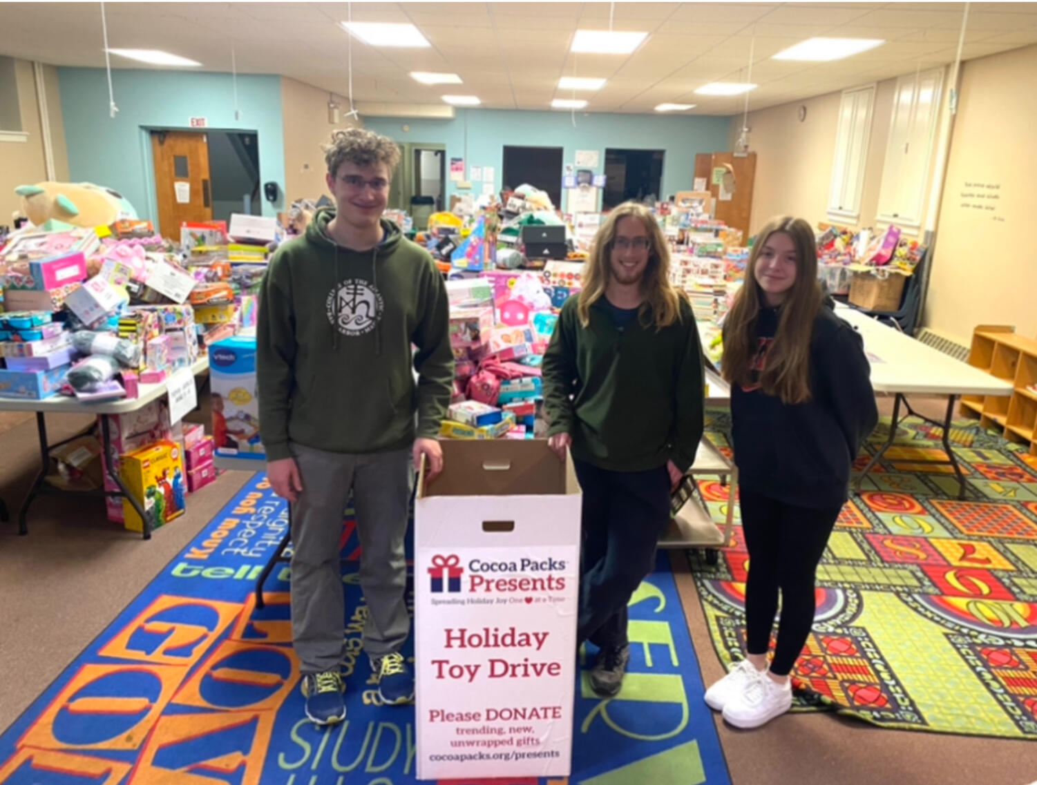 Image file in Basecamp: cutline- Charlie Griffith (junior), Finnian Sieg (senior), and Myra Elliott (junior) pose with a Cocoa Packs Presents toy donation bin. Donation bins were set at different businesses throughout the county during November and the beginning of December.
